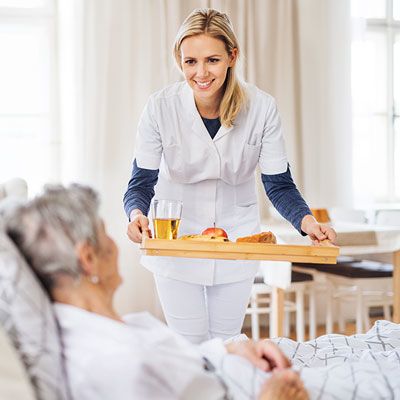 Pflegedienst hilft pflegebedürftiger Frau beim Frühstück 
